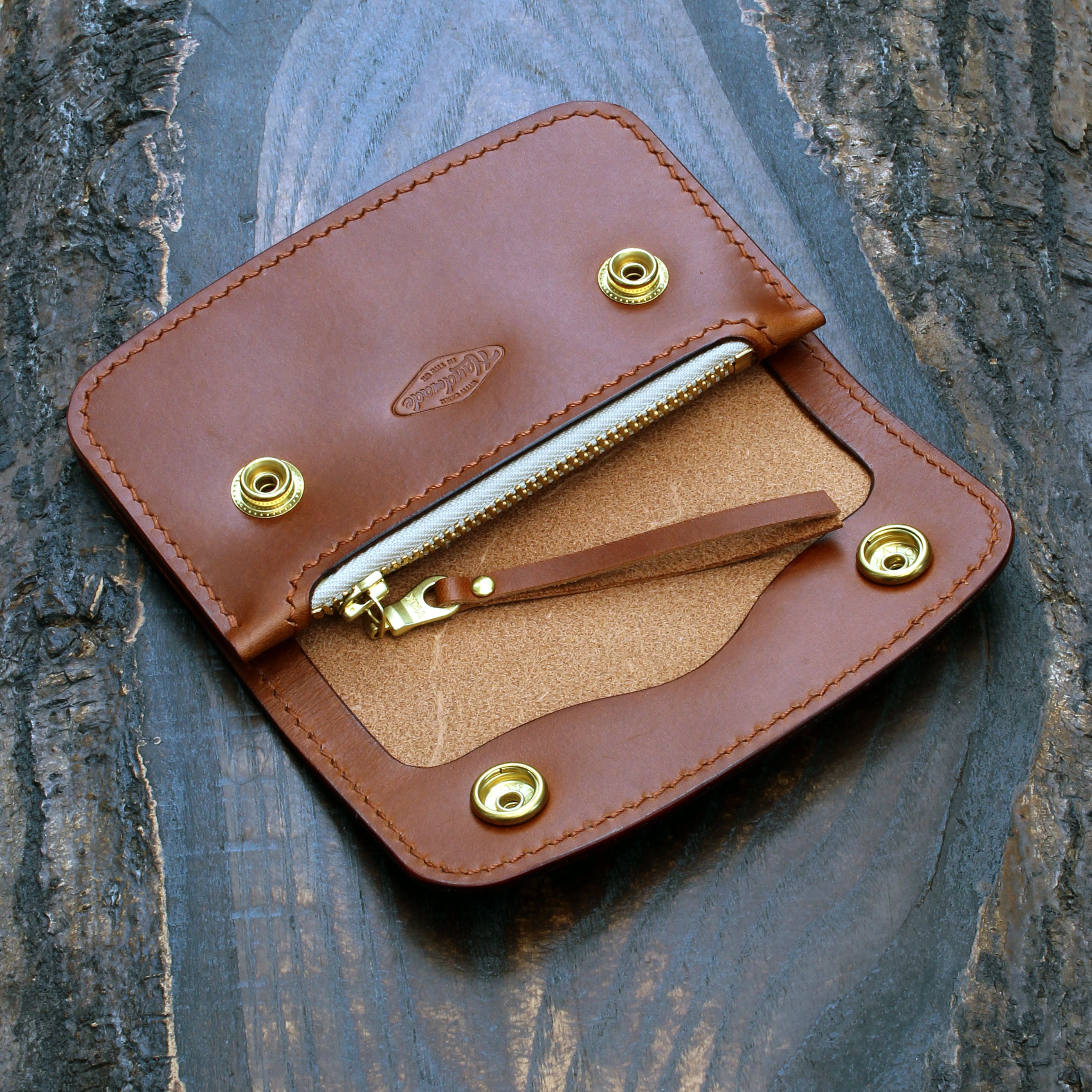 A tan, whiskey Buttero leather short trucker wallet with brass snaps on a wooden surface.
